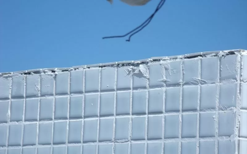 Parede revestida com azulejos brancos danificados.