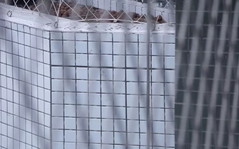 Parede de azulejos brancos com rede de proteção.