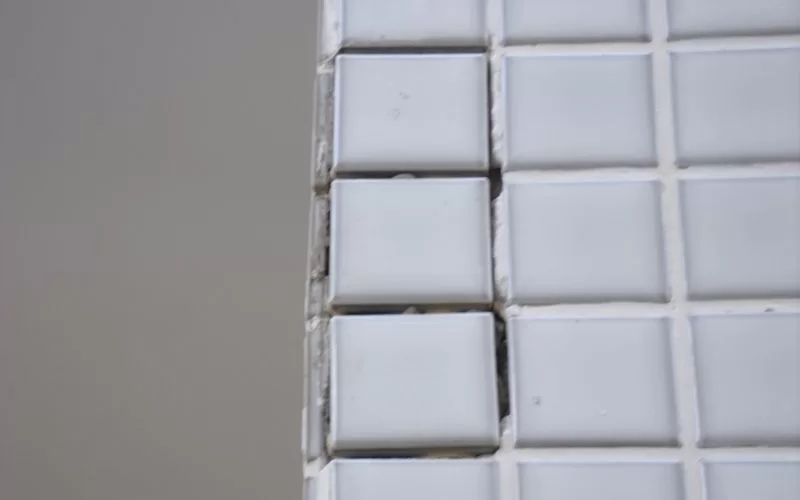 Azulejos brancos desalinhados em parede cinza.