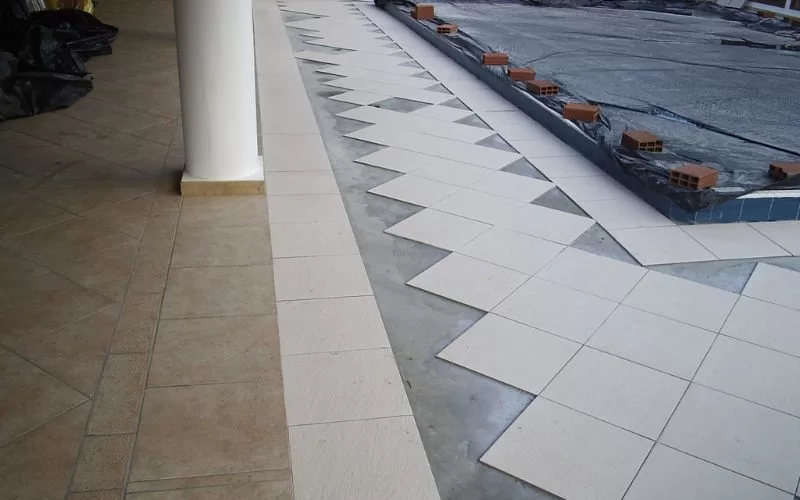 Construção de piso com ladrilhos brancos em progresso.