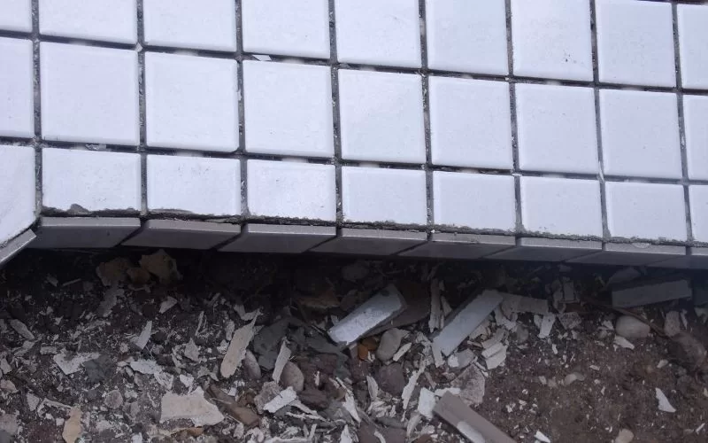 Azulejos brancos danificados sobre chão de escombros.