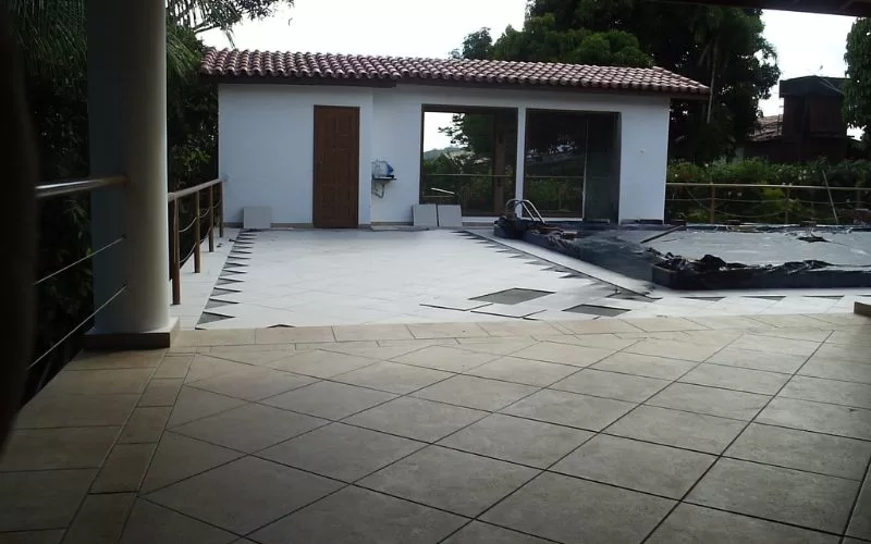 Pátio com piscina em construção e casa ao fundo.