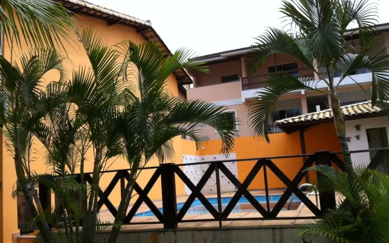Piscina em hotel com palmeiras, edifícios amarelos.