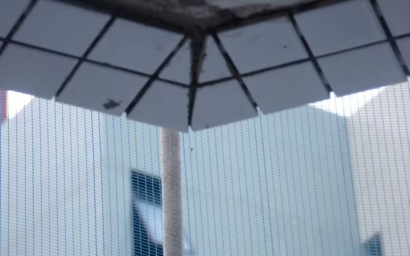 Canto de parede com azulejos faltando, rede protetora.