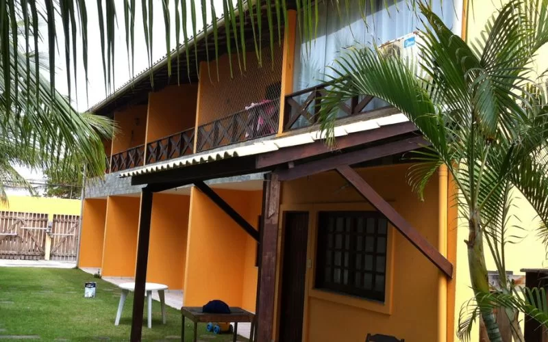 Prédio amarelo com varanda cercada e jardim tropical.