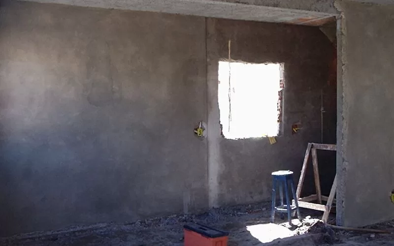 Parede de cimento inacabada com janela no canteiro.