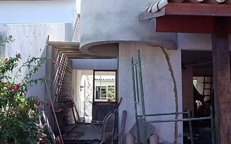 Casa em construção com andaimes e vegetação.