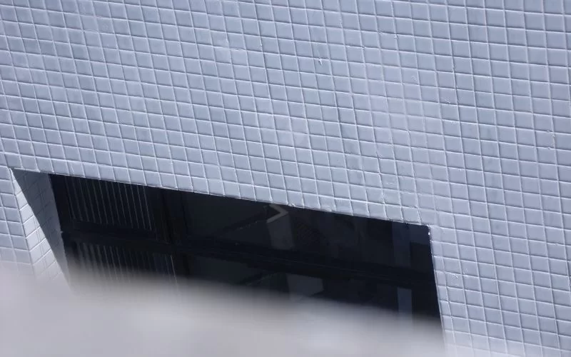 Parede azulejada com janela escura ao fundo.
