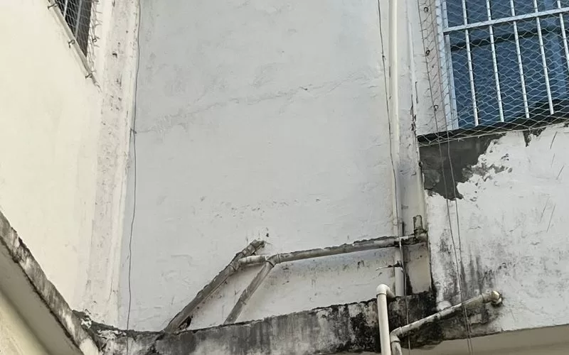 Parede exterior com tubos desgastados e janela gradeada.