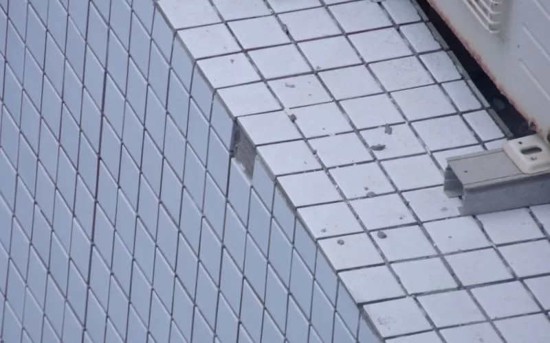 Parede com azulejos brancos danificados.