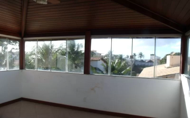 Varanda envidraçada com vista para palmeiras e casas.