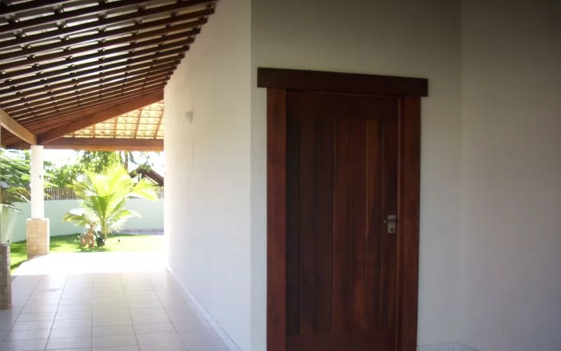 Corredor coberto com porta e jardim ao fundo.