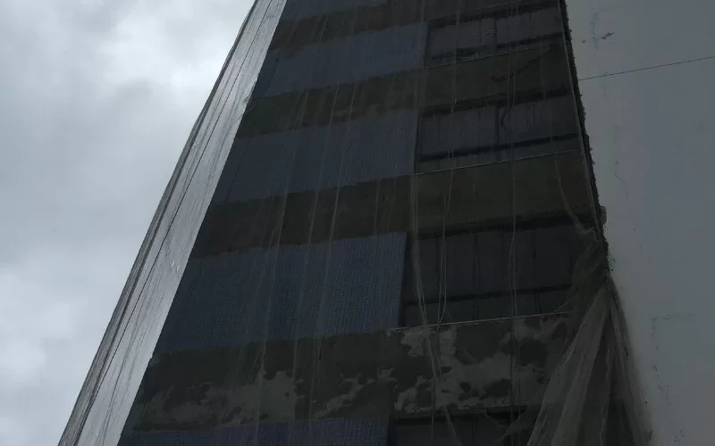 Prédio alto com fachada coberta por rede de segurança.