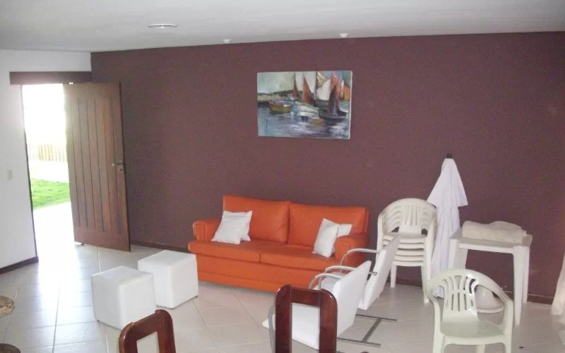 Sala com sofá laranja e cadeiras de plástico.