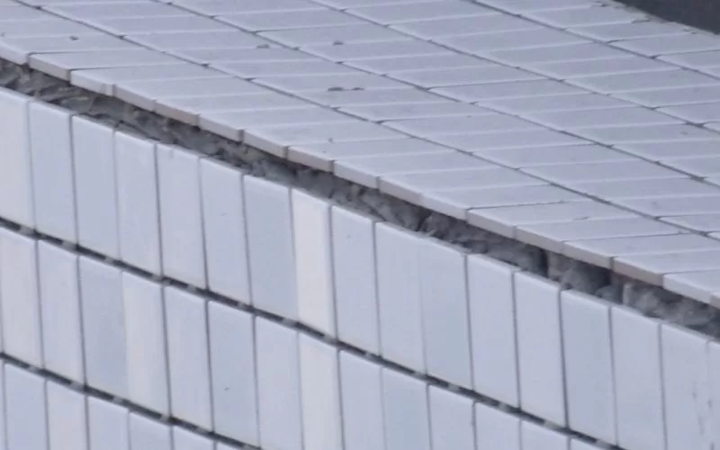 Azulejos brancos desgastados com danos estruturais visíveis.