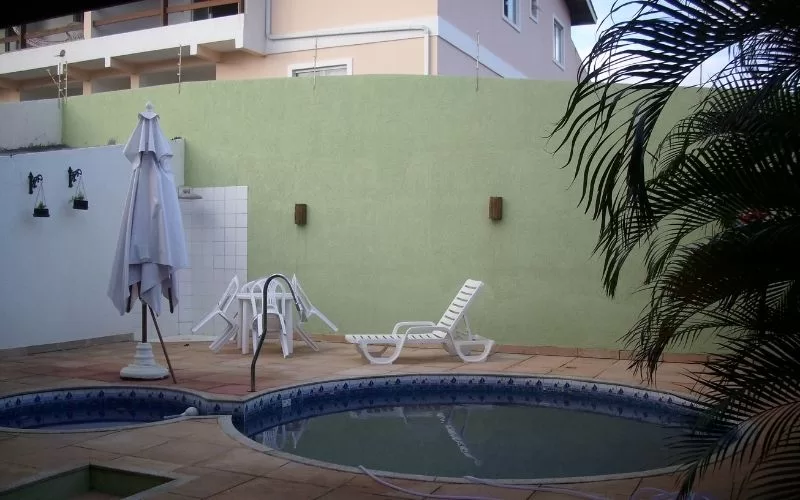 Piscina no pátio com espreguiçadeiras e guarda-sol branco.