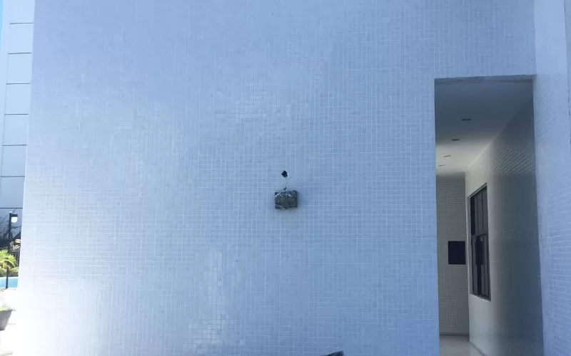 Parede branca com detalhe de azulejo danificado.