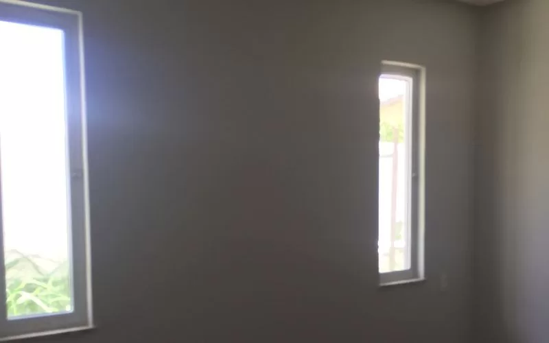 Quarto vazio com duas janelas à luz do dia.