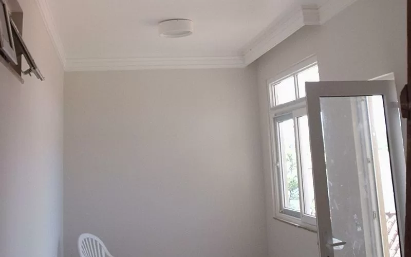 Quarto vazio com janela e cadeiras plásticas brancas.