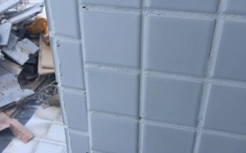 Parede com azulejos brancos danificados.