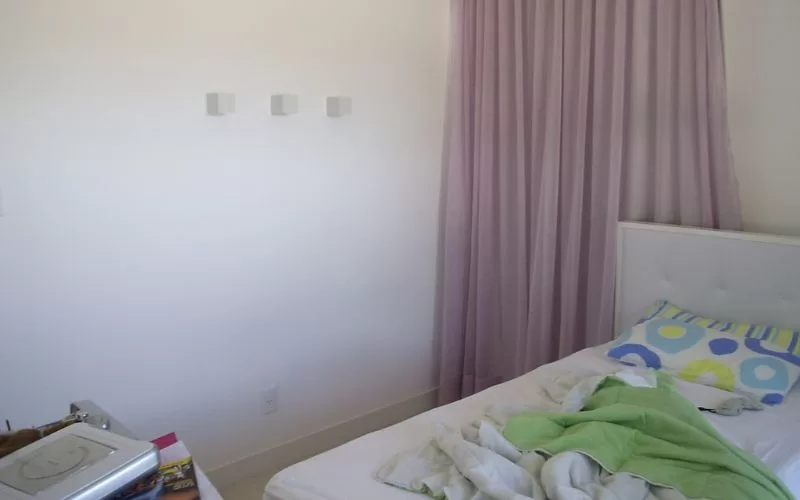 Quarto desarrumado com cortinas lilases e cama desfeita.