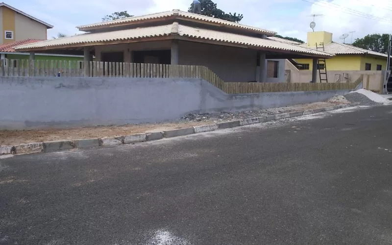 Casa em construção com muro e telhado concluídos.