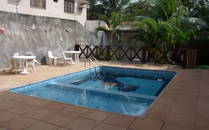 Piscina exterior com mesas e cadeiras brancas.