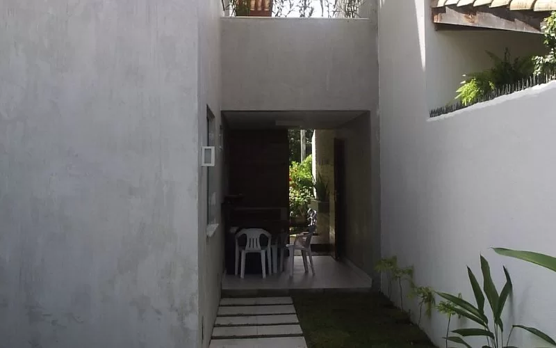 Corredor externo com jardim e cadeiras brancas.