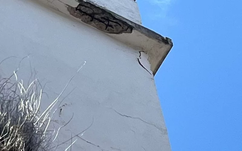 Rachaduras em edifício com céu azul ao fundo.