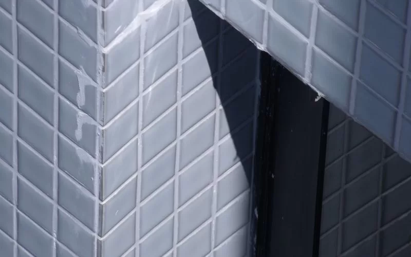 Parede de azulejos cinzentos com sombra diagonal.