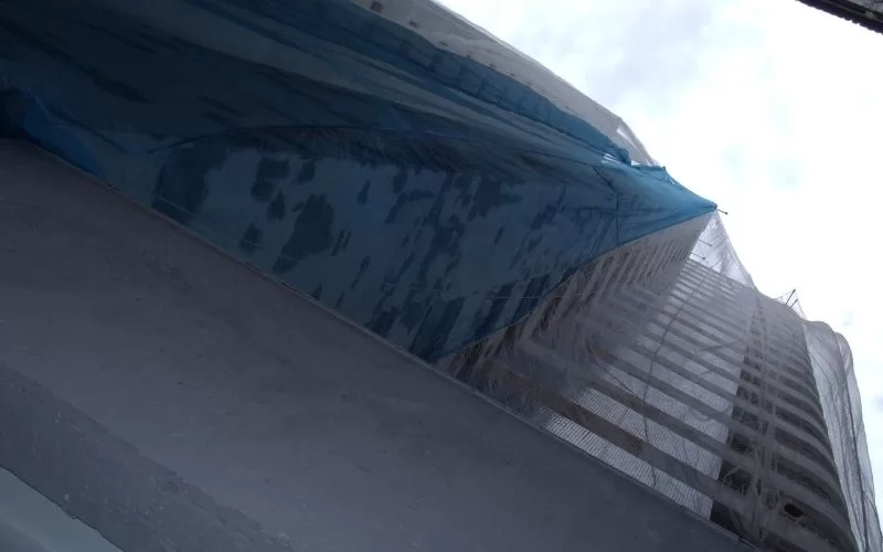 Edifício em construção com rede azul visível.