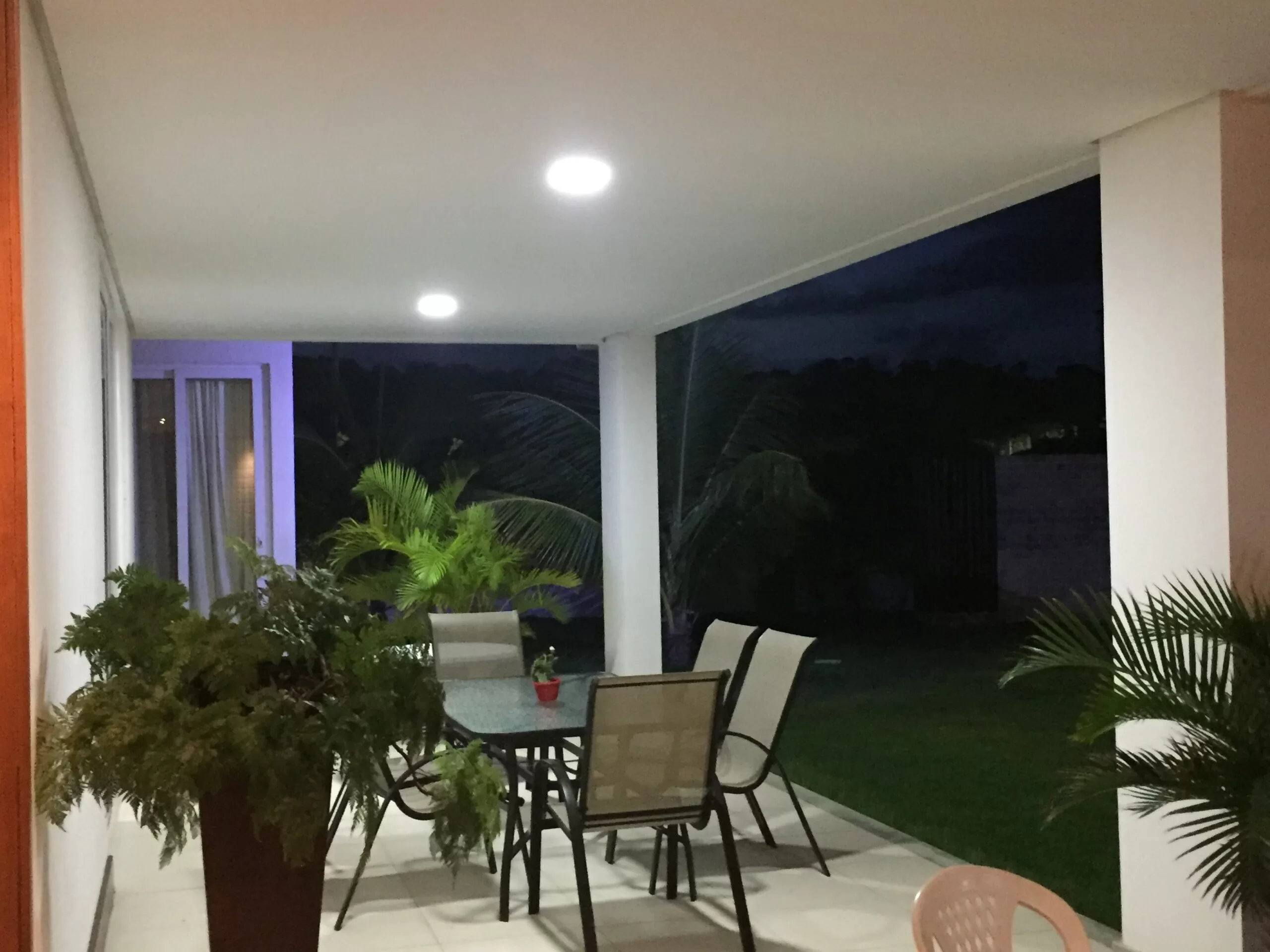Varanda iluminada com plantas e mesa ao anoitecer.