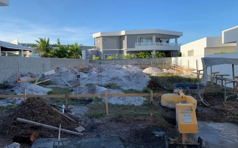 Terreno em construção residencial com casas ao fundo.