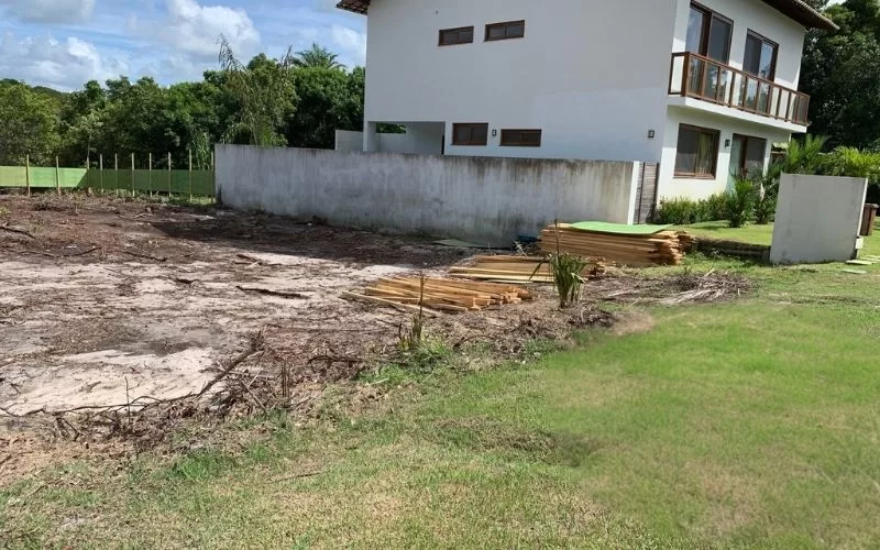 Terreno com madeira ao lado de casa branca.