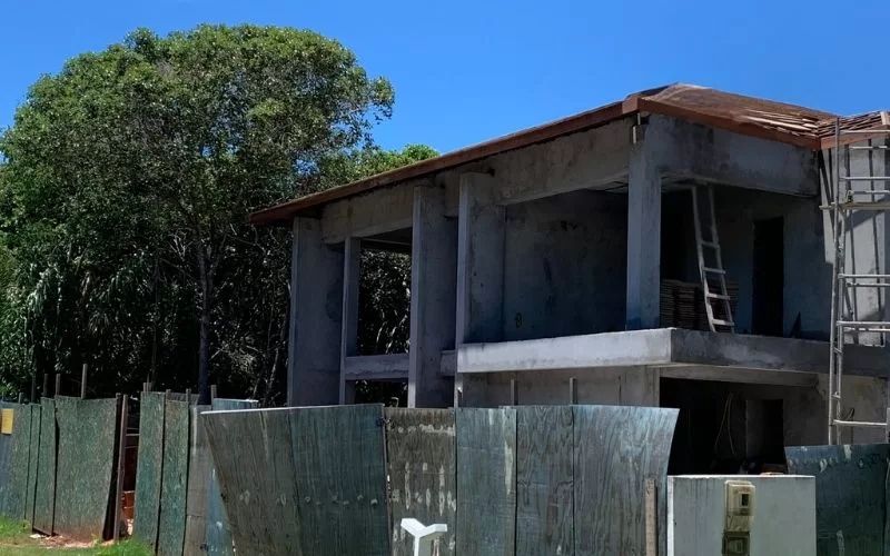 Construção de casa inacabada ao lado de árvores verdes.