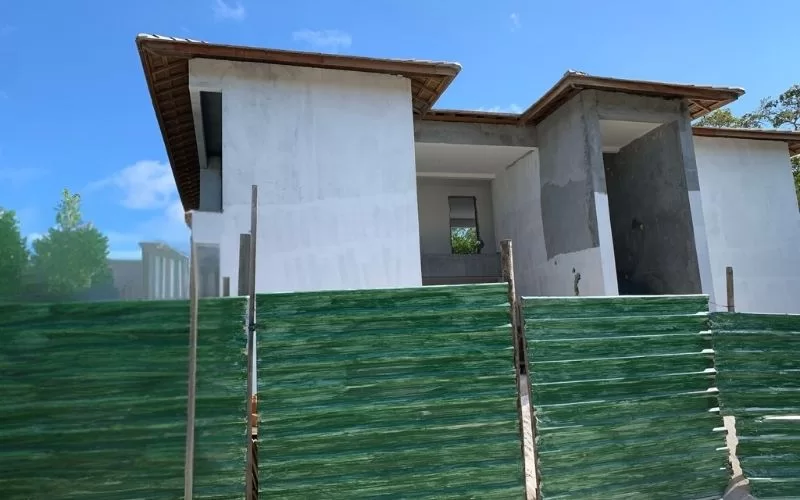 Casa em construção com cerca verde.