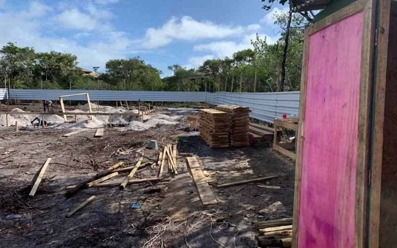 Local de construção com materiais e floresta ao fundo.