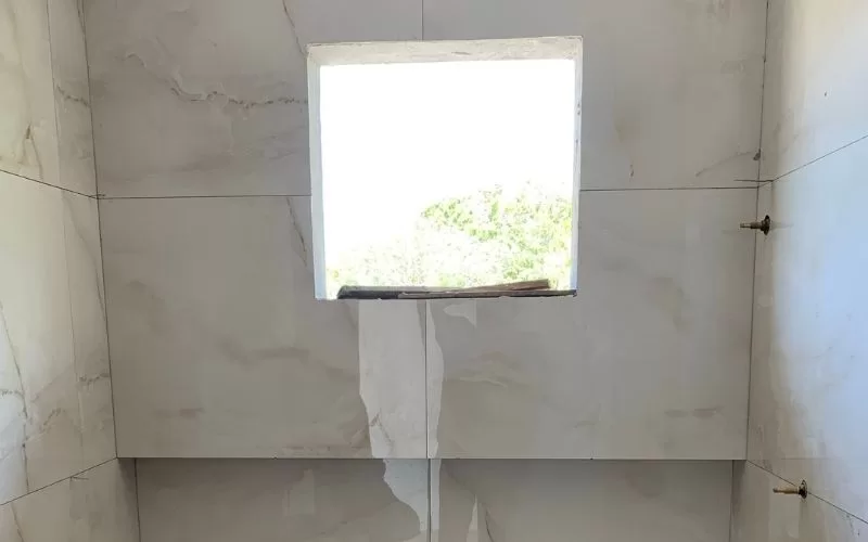 Casa de banho com azulejos e janela quadrada.