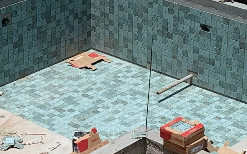 Construção de piscina com azulejos azuis quadrados.