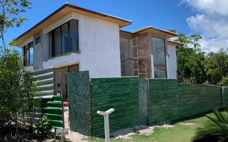 Casa em construção com cerca verde ao redor.
