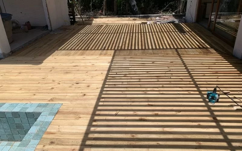 Deck de madeira com sombras e piscina verde-azul.