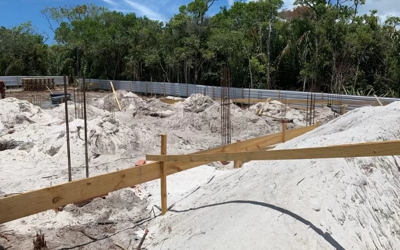 Terreno em construção com areia e vegetação ao fundo.