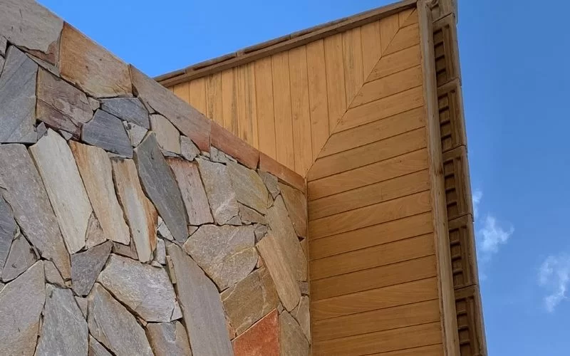Parede de pedra e madeira sob céu azul.