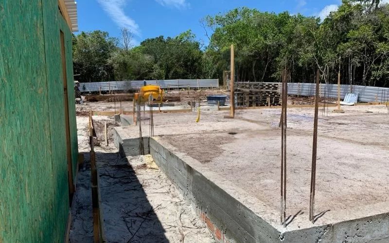 Terreno em construção com concreto e árvores ao fundo.