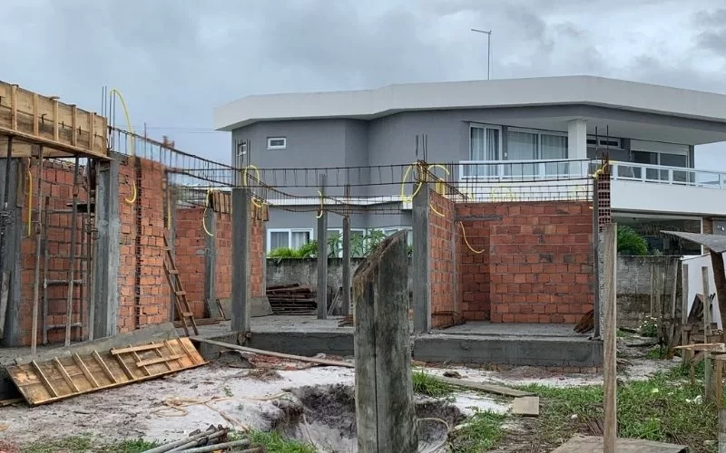 Construção em andamento com casa ao fundo.