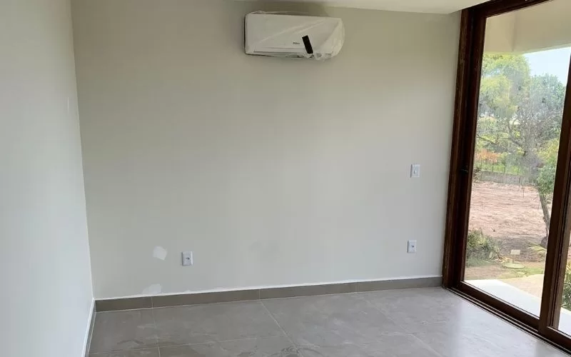 Quarto vazio com ar condicionado e janela grande.