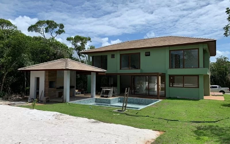 Casa moderna com piscina em construção, rodeada de árvores.