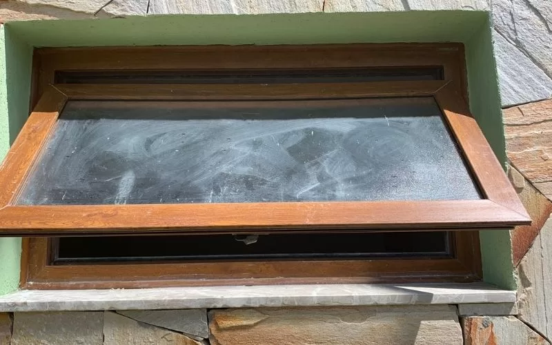 Janela basculante aberta em parede de pedra.