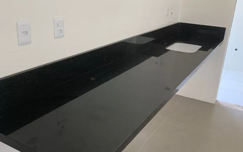 Bancada de cozinha em granito preto com lavatório.
