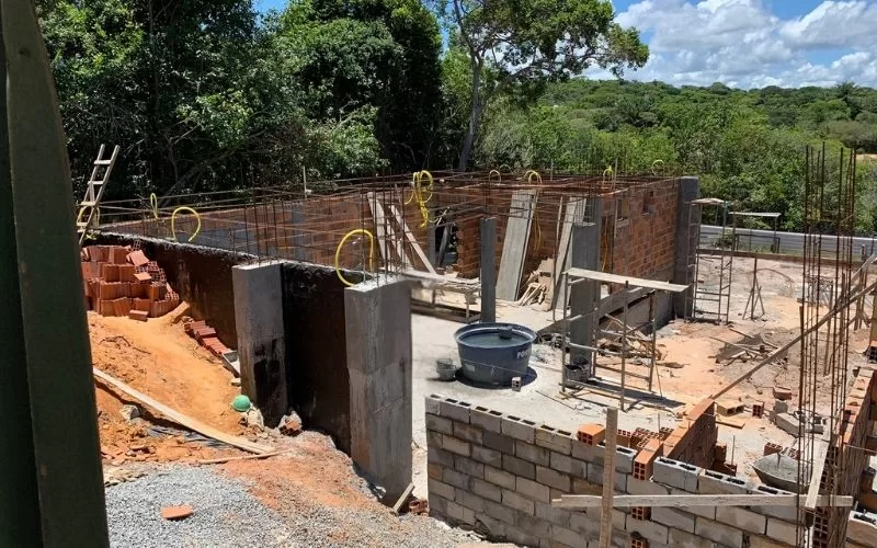 Construção de casa em andamento com floresta ao fundo.